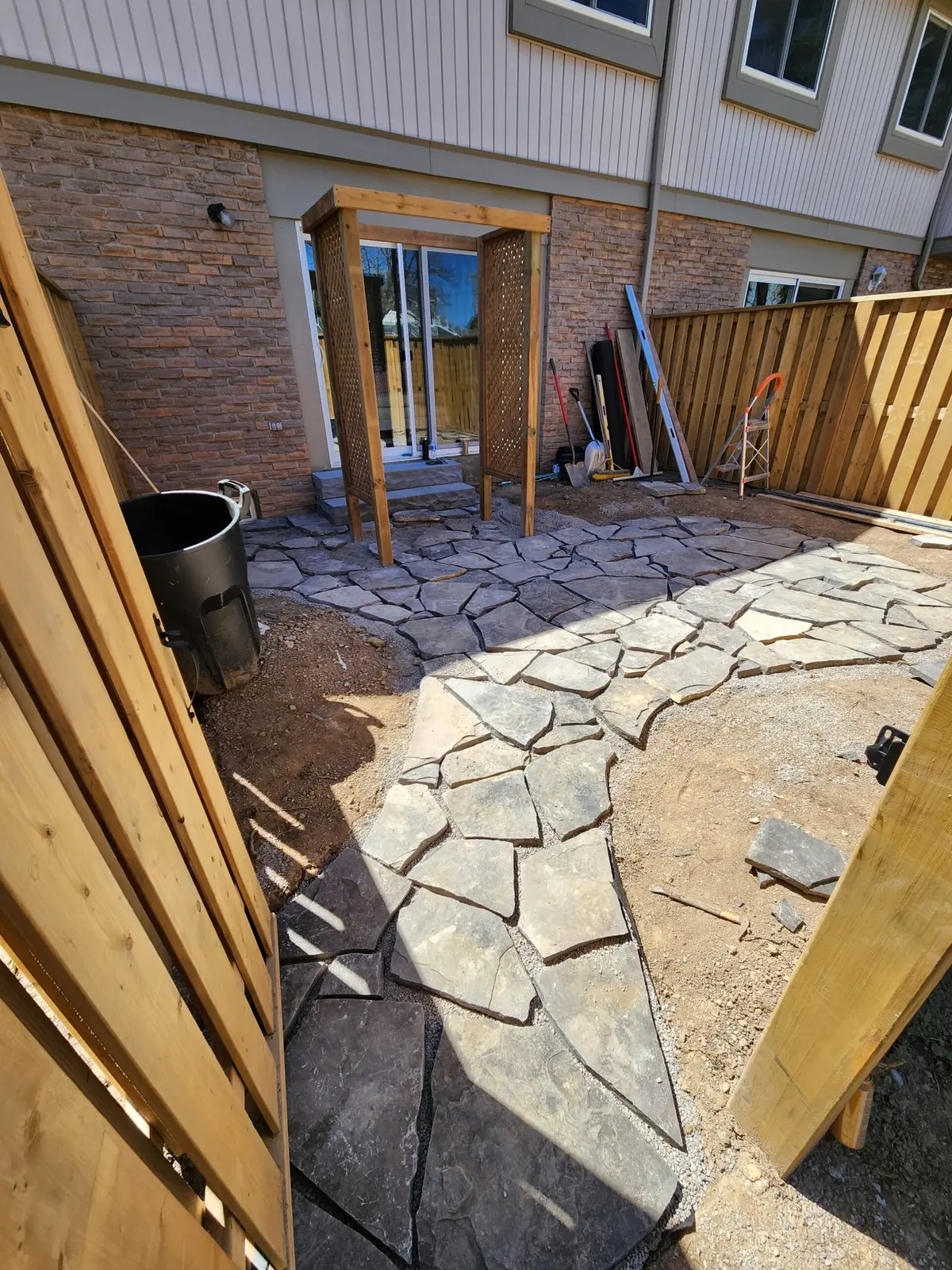 Flagstone patio installation in progress with cedar fence surround