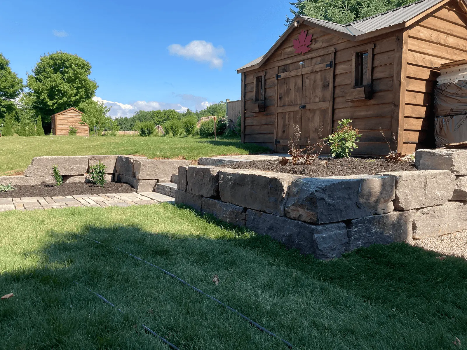 Armour stone retaining wall with raised garden bed beside rustic shed